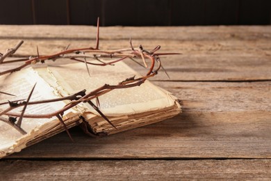 Photo of Crown of thorns and Bible on wooden table, closeup. Space for text