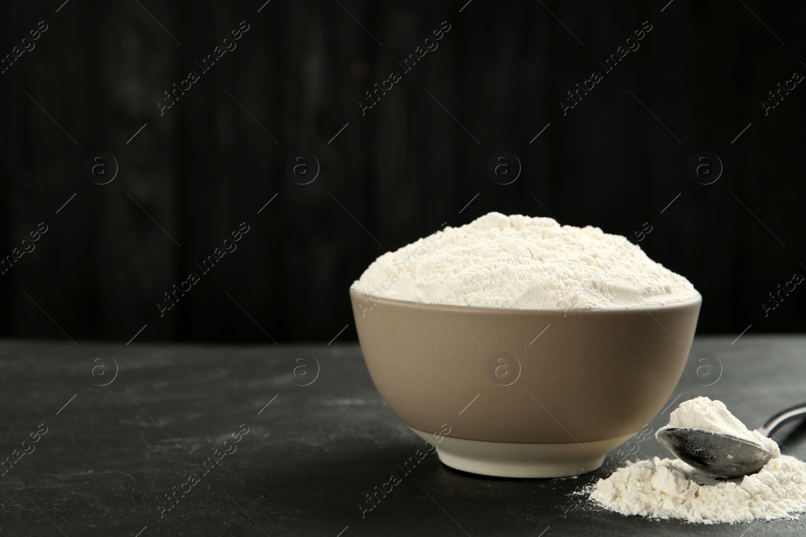 Photo of Ceramic bowl with flour on dark grey table, space for text. Cooking utensils