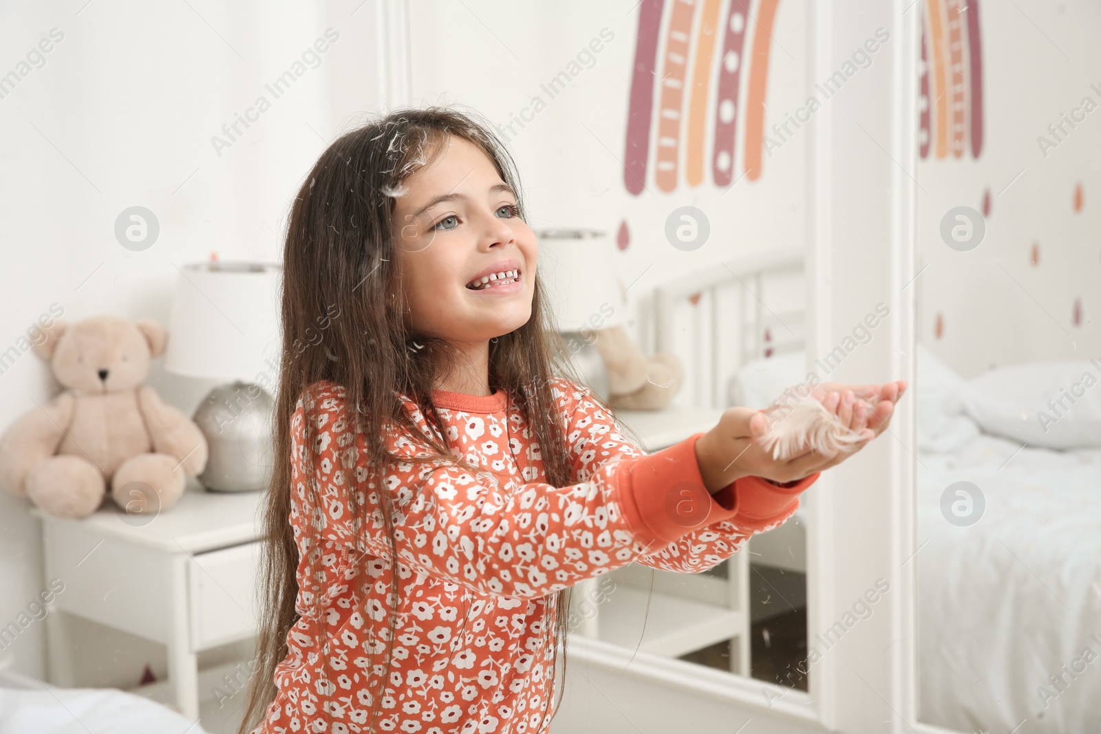 Photo of Cute little girl in pajamas playing with feathers at home. Happy childhood