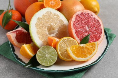 Photo of Plate with different citrus fruits and fresh leaves on light grey table, closeup