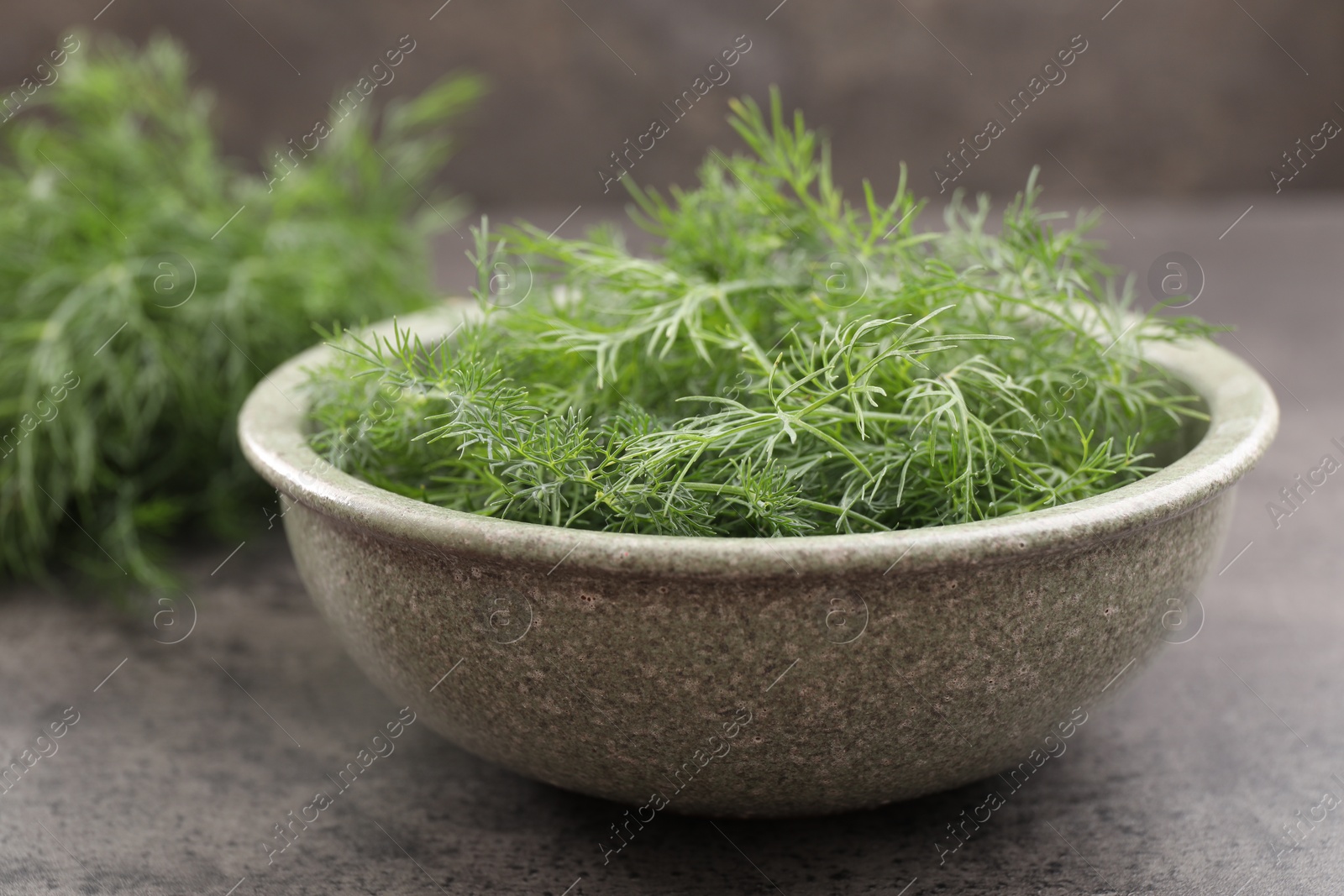 Photo of Bowl of fresh dill on grey table, closeup