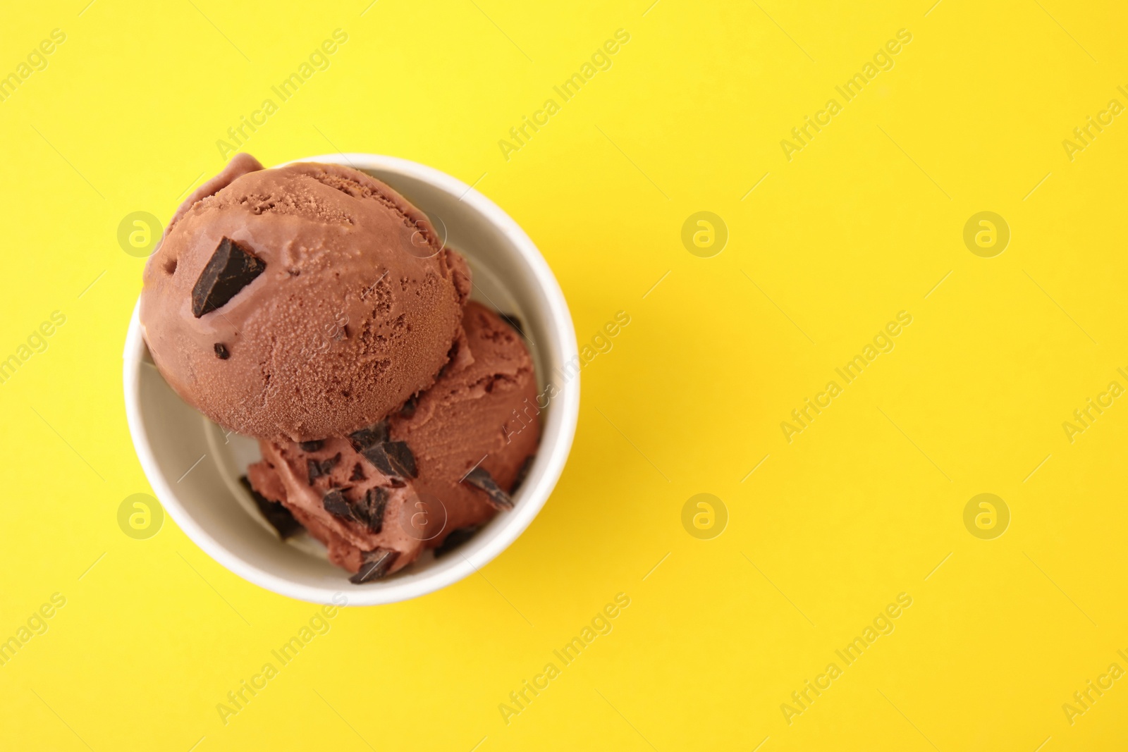 Photo of Cup with tasty chocolate ice cream on yellow background, top view. Space for text