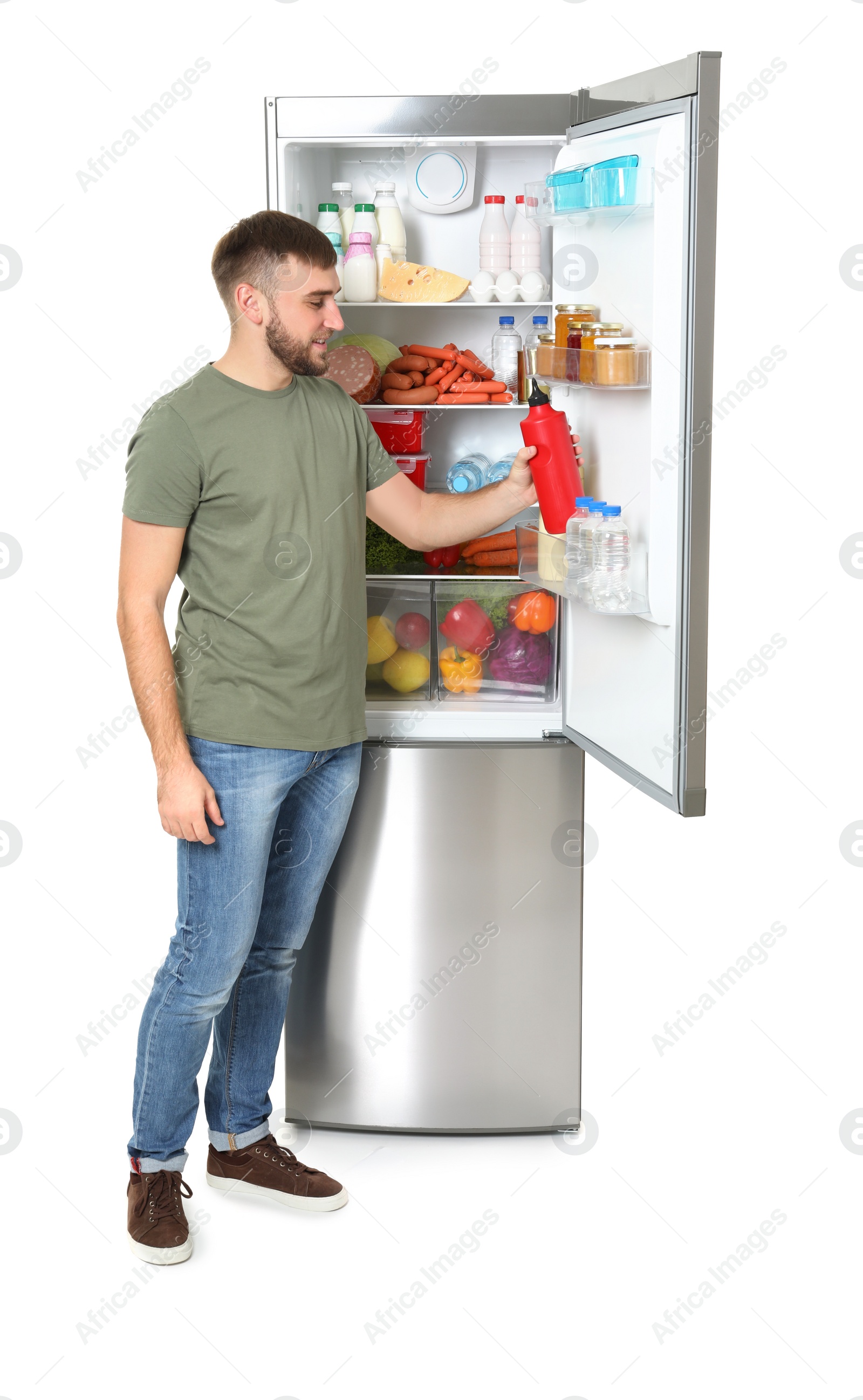 Photo of Young man taking bottle of ketchup from refrigerator on white background