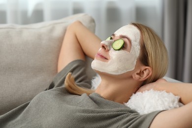 Young woman with face mask and cucumber slices resting on sofa at home. Spa treatments