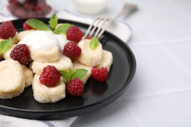 Photo of Plate of tasty lazy dumplings with raspberries, sour cream and mint leaves on white tiled table, closeup. Space for text