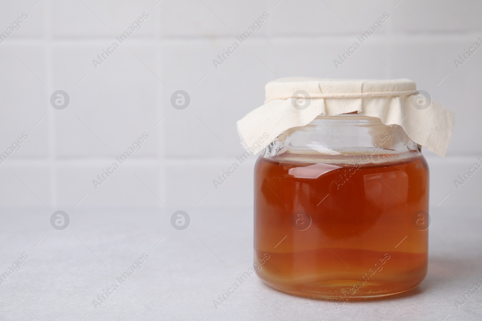 Photo of Tasty kombucha in glass jar on white table, space for text