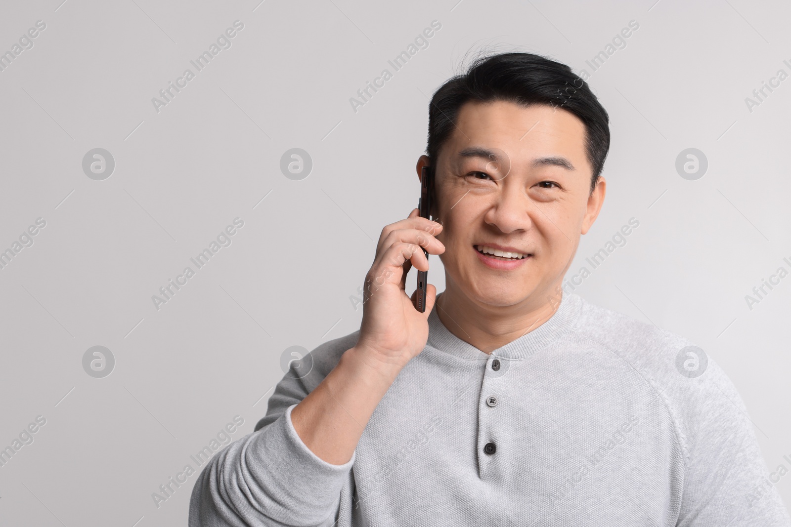 Photo of Portrait of happy man talking by smartphone on light background. Space for text