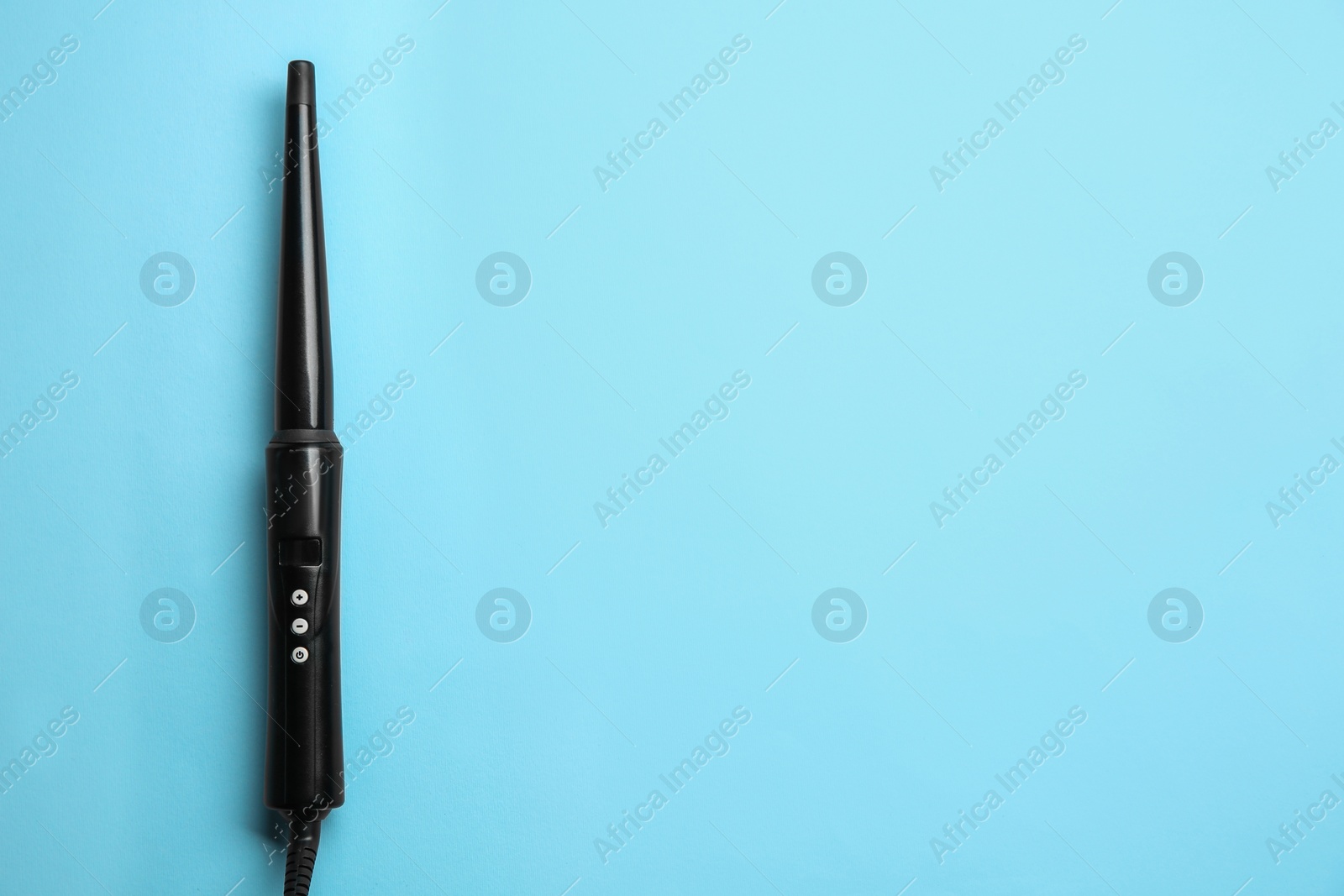 Photo of Modern clipless curling hair iron on light blue background, top view. Space for text
