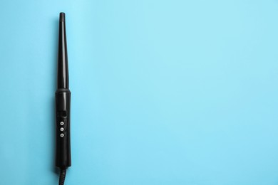 Modern clipless curling hair iron on light blue background, top view. Space for text