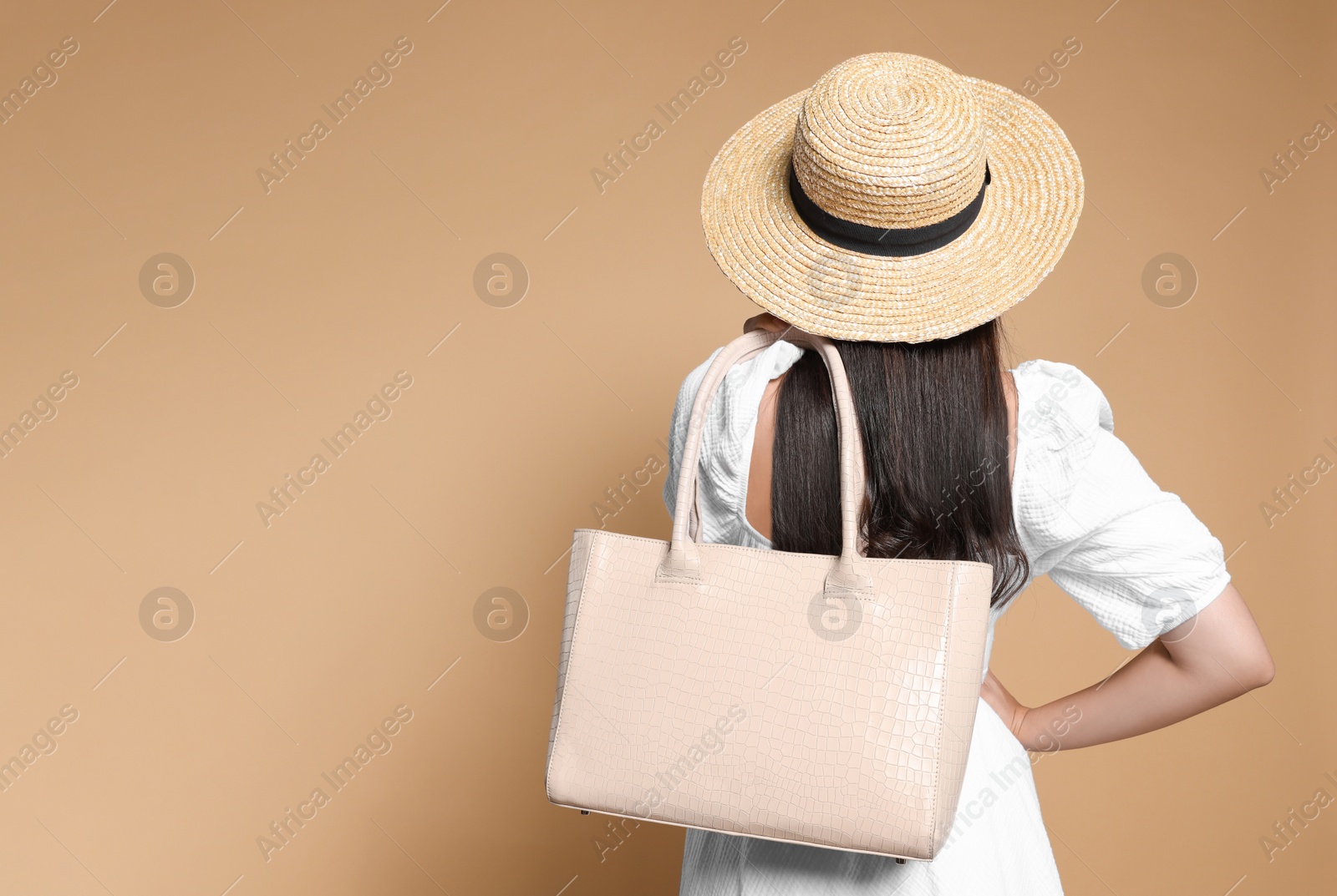 Photo of Young woman with stylish bag on beige background, back view. Space for text