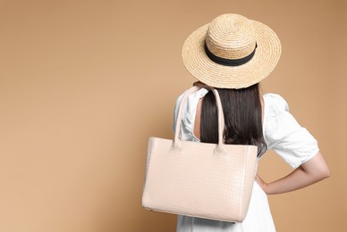 Photo of Young woman with stylish bag on beige background, back view. Space for text