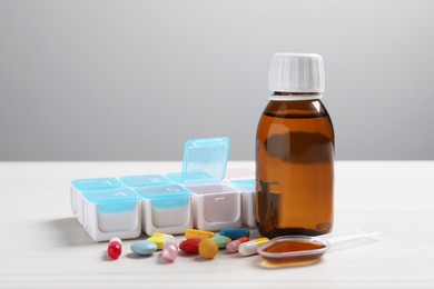 Photo of Bottle of syrup, dosing spoon and pills on white table against light grey background. Cold medicine