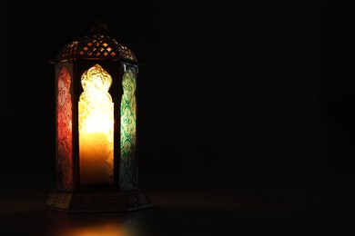 Photo of Decorative Arabic lantern on table against black background, space for text