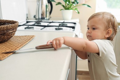 Little child holding sharp knife in kitchen. Dangerous situation