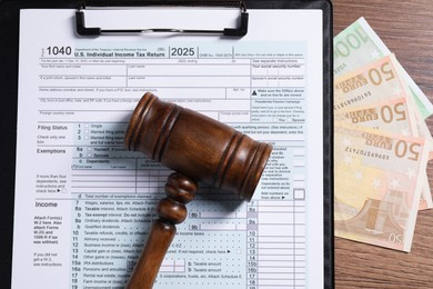 Photo of Tax return form, euro banknotes and gavel on wooden table, top view
