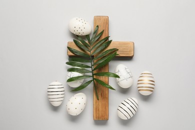 Wooden cross, painted Easter eggs and palm leaf on light grey background, flat lay