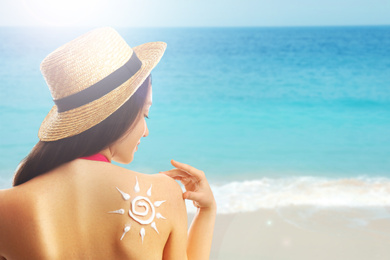 Young woman with sun protection cream on her back at beach, space for text