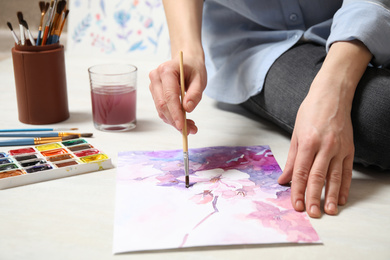 Woman painting flowers with watercolor on floor, closeup