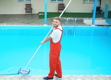 Photo of Male worker cleaning outdoor pool with underwater vacuum