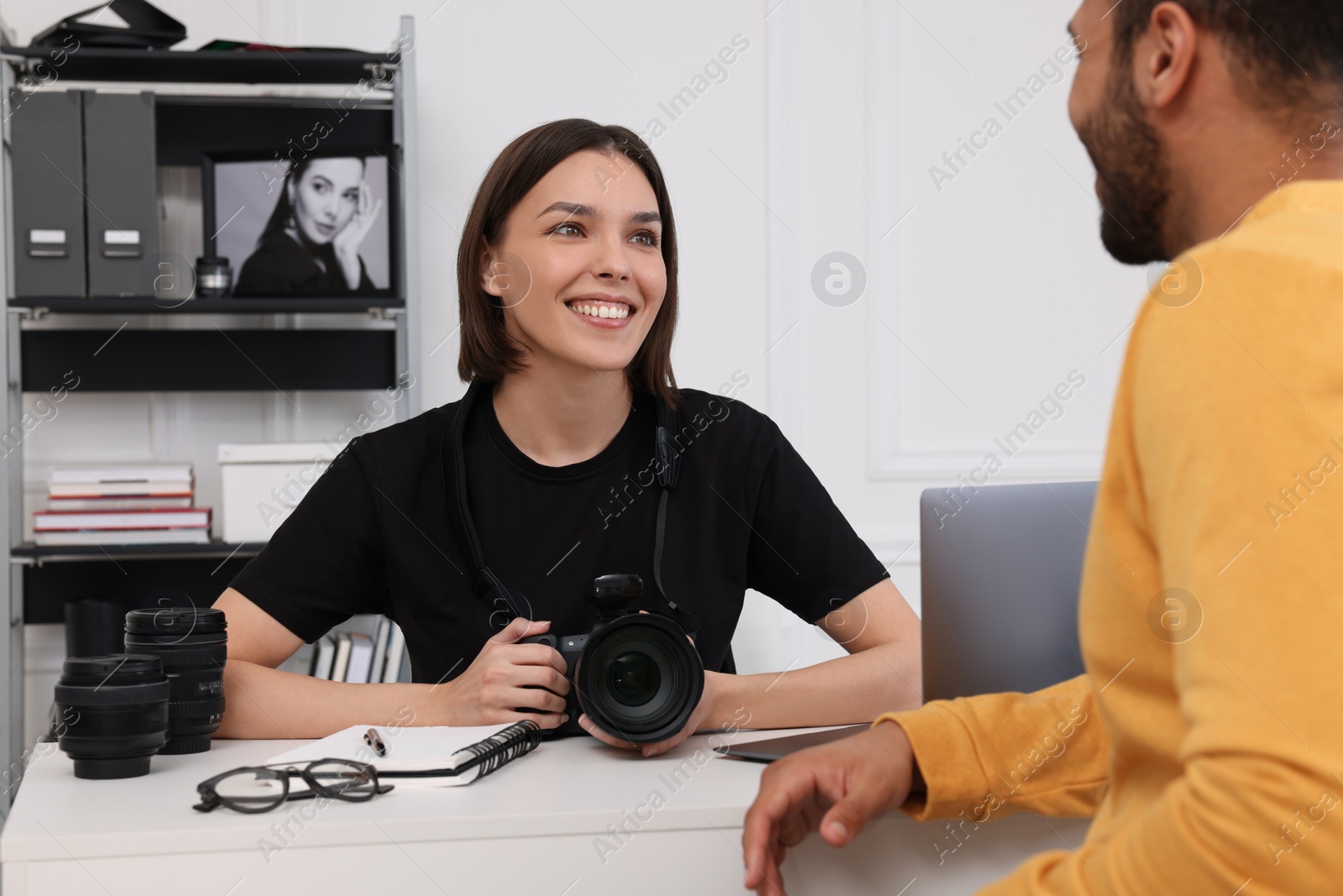 Photo of Young professional photographer holding camera while talking with man in modern photo studio