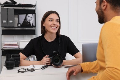 Young professional photographer holding camera while talking with man in modern photo studio