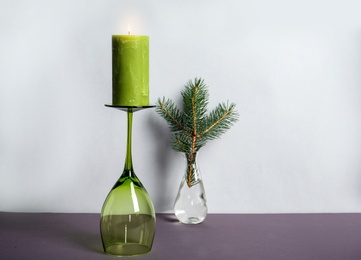 Photo of Decorative wax candle and wineglass on table against light background