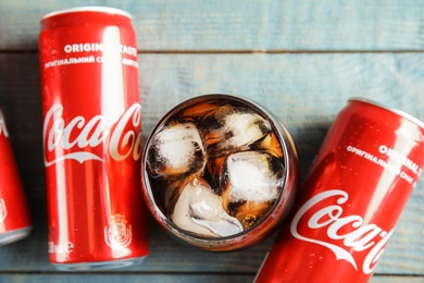 Photo of MYKOLAIV, UKRAINE - NOVEMBER 15, 2018: Cans and glass with Coca Cola on wooden table, top view