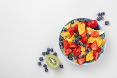 Yummy fruit salad in bowl and ingredients on light grey background, flat lay. Space for text
