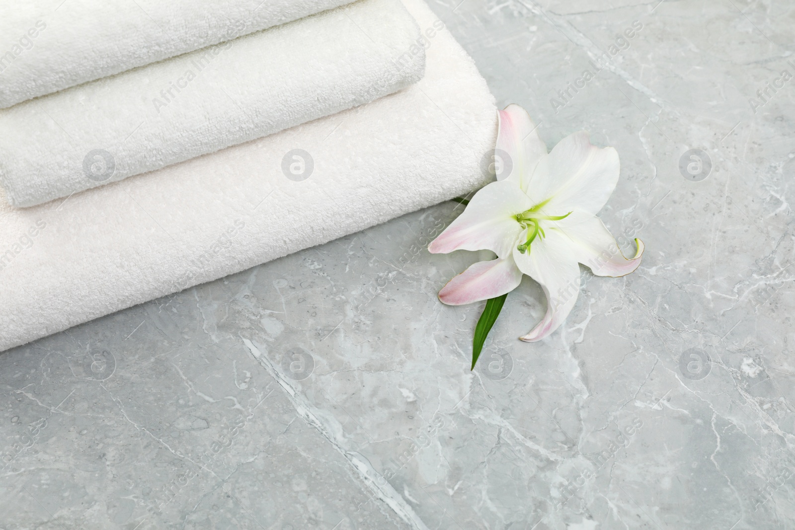 Photo of Stack of fresh towels with flower on grey table, above view. Space for text