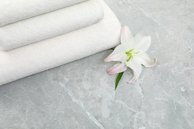 Photo of Stack of fresh towels with flower on grey table, above view. Space for text