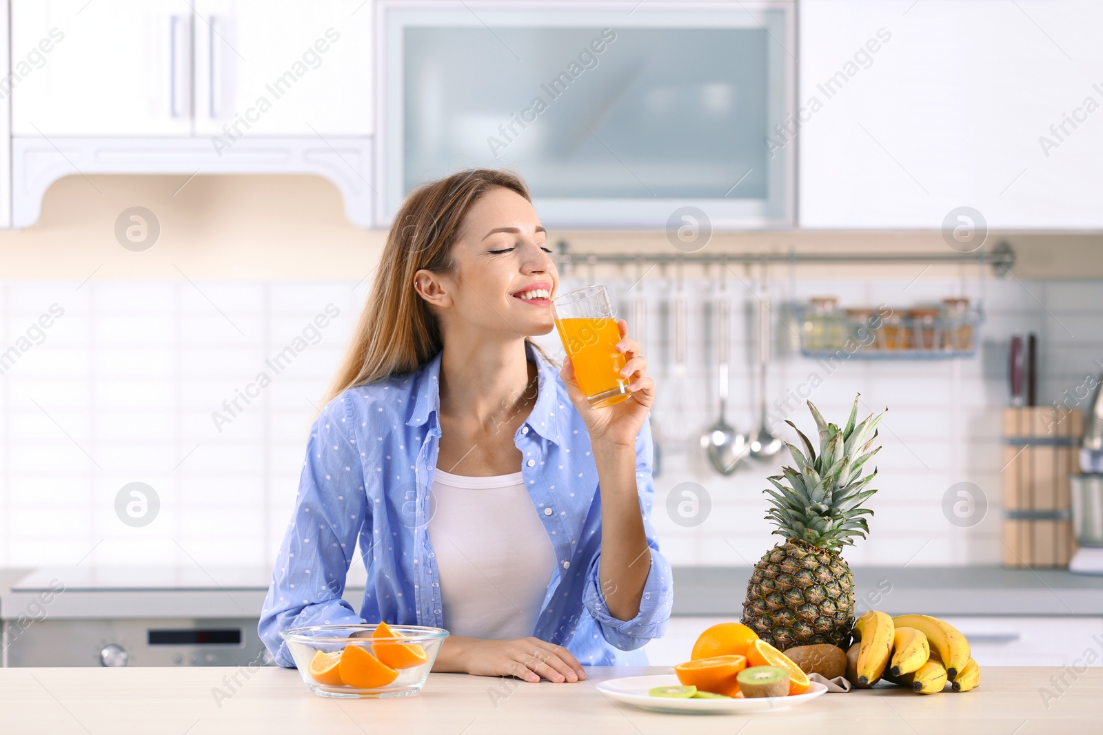 Photo of Woman with glass of orange juice at table in kitchen. Healthy diet