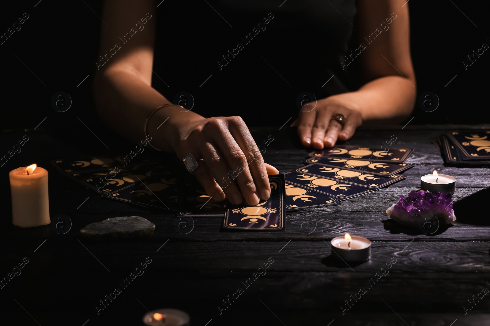 Photo of Soothsayer predicting future with tarot cards at table in darkness, closeup