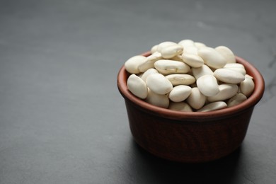 Raw white beans in bowl on black table. Space for text