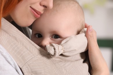 Photo of Mother holding her child in sling (baby carrier) against blurred background, closeup