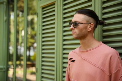Photo of Handsome young man in stylish sunglasses near shutters outdoors, space for text