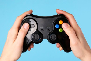 Photo of Woman using game controller on light blue background, closeup