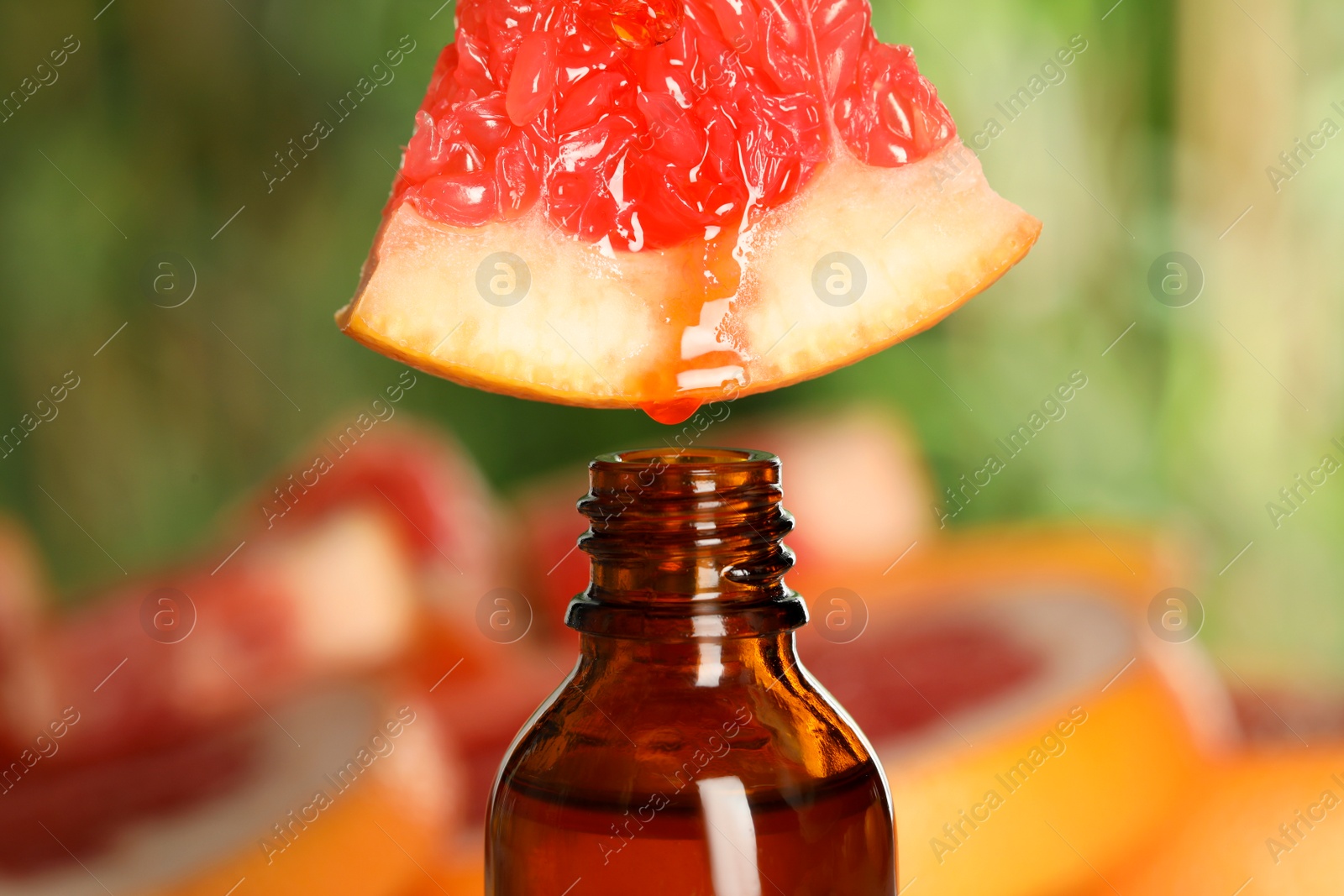 Photo of Dripping essential oil from grapefruit into bottle on blurred background, closeup