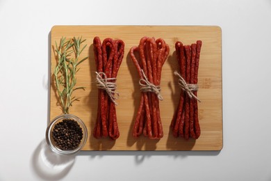 Photo of Bundles of delicious kabanosy with rosemary and peppercorn on white background, top view