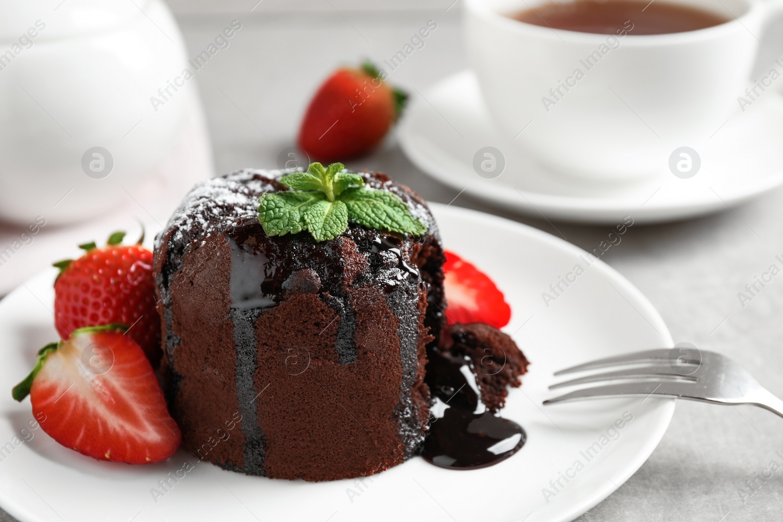 Photo of Delicious warm chocolate lava cake with mint and strawberries on table, closeup