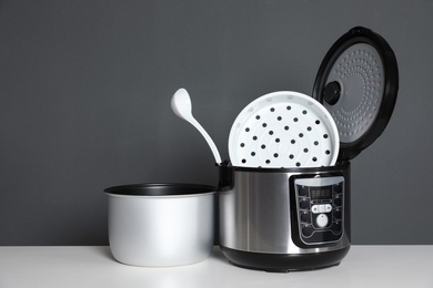 Disassembled electric multi cooker with spoon on table against dark background