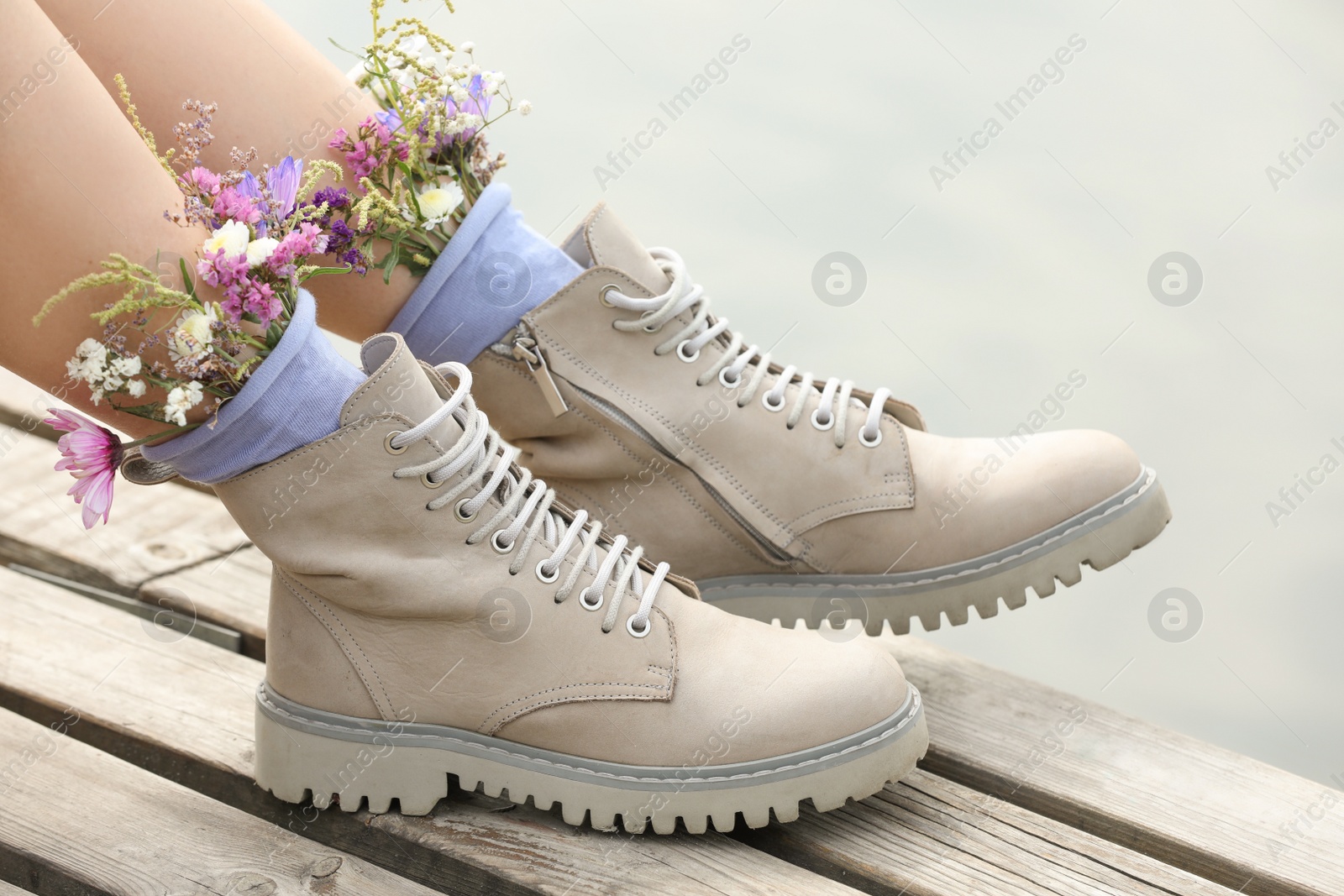 Photo of Woman sitting on wooden pier with flowers in socks outdoors, closeup