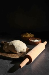 Photo of Rolling pin, flour and dough on black table