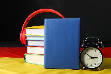 Photo of Learning foreign language. Different books, alarm clock and headphones on flag of Germany