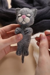 Photo of Woman felting cute toy cat from wool at beige table, closeup