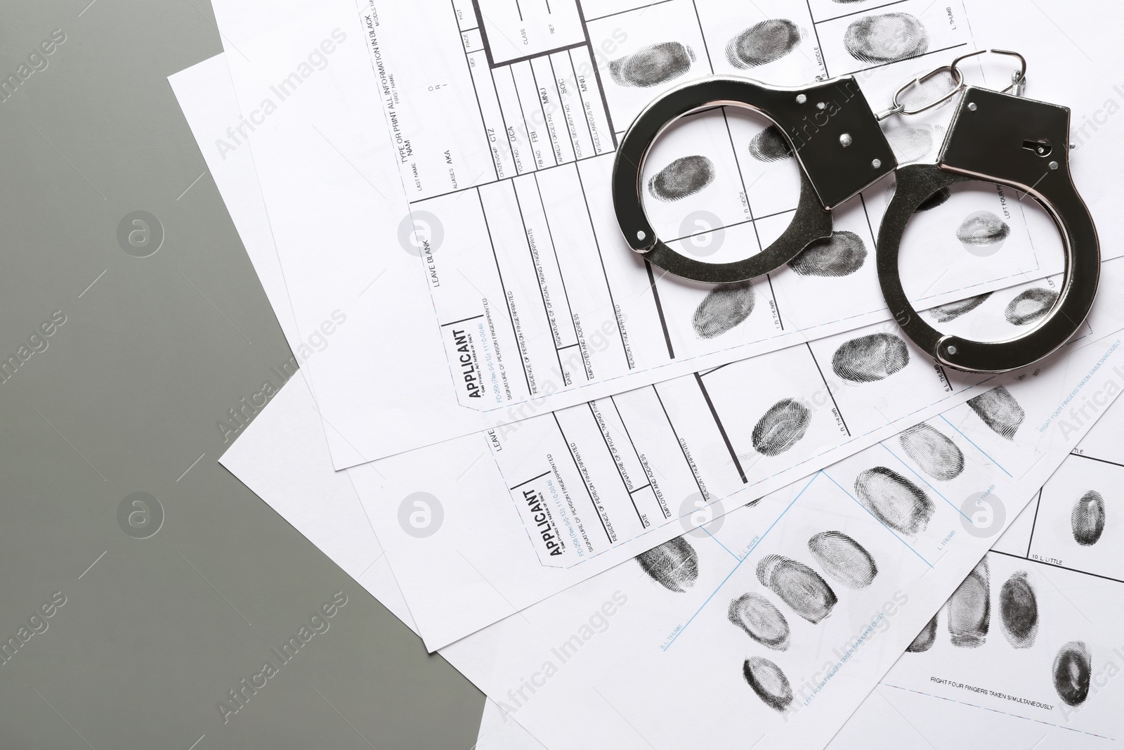 Photo of Handcuffs and fingerprint record sheets on grey background, space for text. Criminal investigation