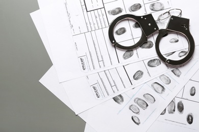 Photo of Handcuffs and fingerprint record sheets on grey background, space for text. Criminal investigation