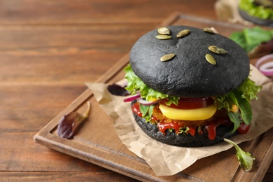 Photo of Board with tasty black vegetarian burger on wooden table