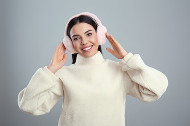 Photo of Beautiful young woman wearing earmuffs on light grey background