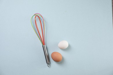 Photo of Colorful whisk and raw eggs on light blue background, flat lay