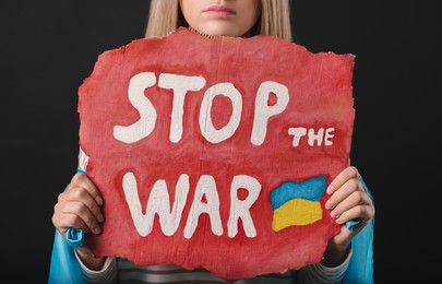 Photo of Sad woman holding poster with words Stop the War on black background, closeup